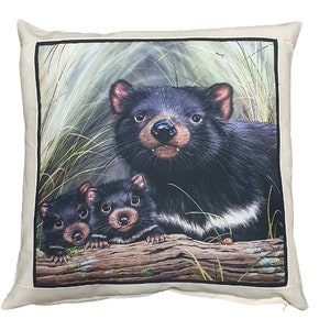 May include: A throw pillow with a printed image of a Tasmanian devil and two young Tasmanian devils. The adult devil is looking directly at the viewer. The background is a green and brown forest scene.