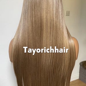 May include: A long, straight wig with a blend of blonde and light brown tones. The hair is styled to fall down the back. The text "Tayorichhair" is displayed across the front of the wig.