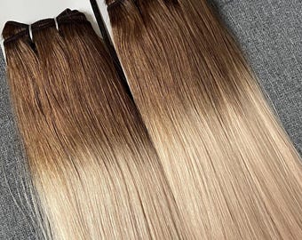 以下が含まれることがあります： 2つの束のグラデーションヘアエクステンション。髪は根元がダークブラウンで、毛先に向かってライトブロンドにフェードしています。