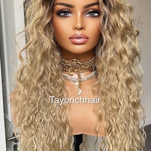 K&ouml;nnte beinhalten: Eine lange, blonde Per&uuml;cke mit lockeren Locken. Die Per&uuml;cke ist mit einem Mittelscheitel gestylt und f&auml;llt bis zu den Schultern. Die Per&uuml;cke sitzt auf einem Mannequin-Kopf mit einer goldenen Halskette.
