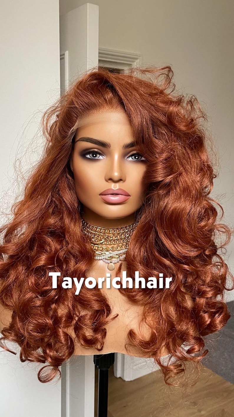 May include: A mannequin head with a copper-colored, curly wig. The wig has a lace front and is styled with voluminous waves. The mannequin is wearing a gold chain necklace. The text "Tayorichhair" is displayed at the bottom.