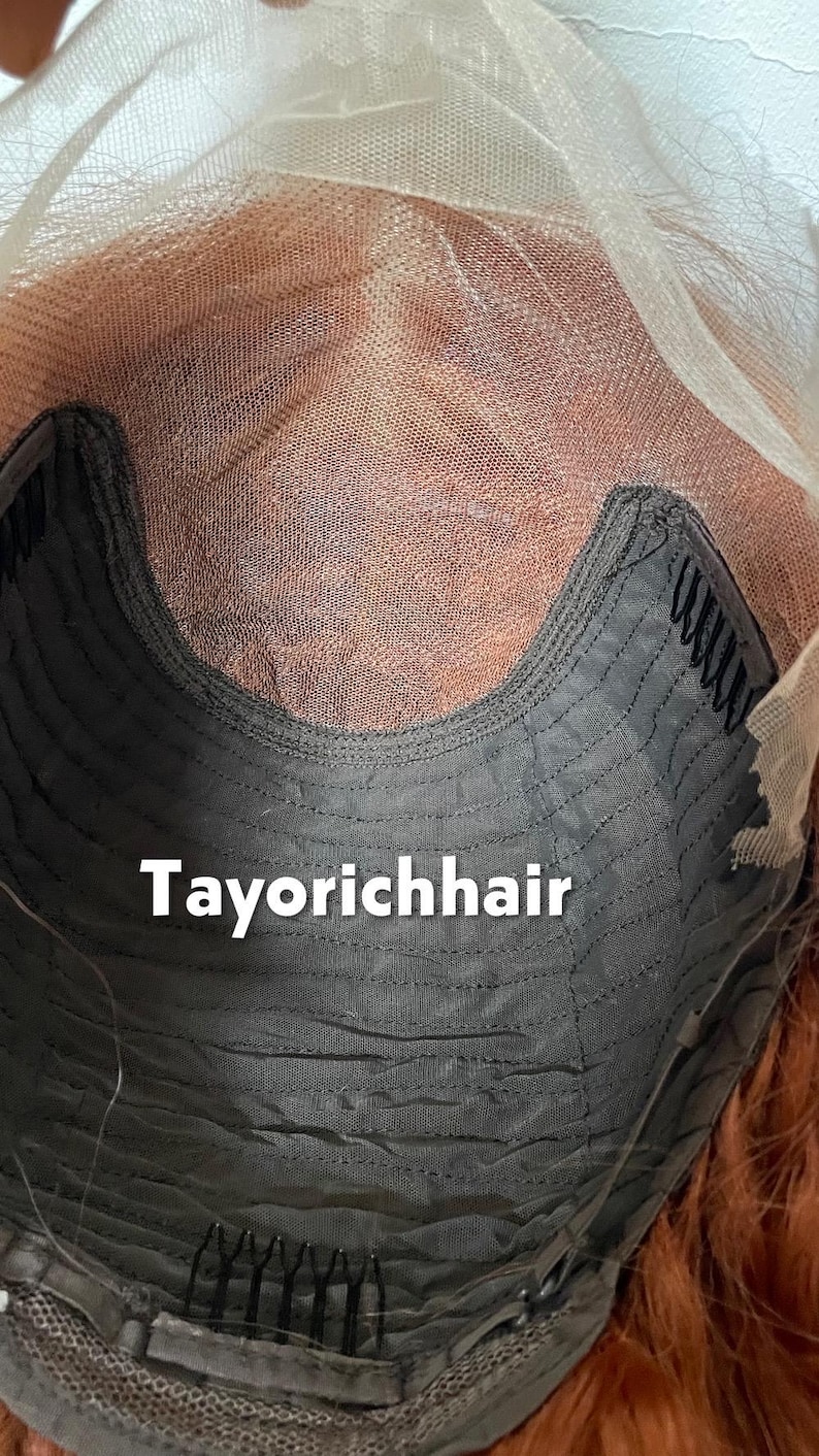 May include: Close-up of a wig cap with the text "Tayorichhair". The cap is dark gray with a curved design and small combs. The wig's lace front is visible, along with the reddish-brown hair.