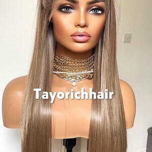 May include: A long, straight, blonde wig on a mannequin head. The wig has a natural-looking hairline and is styled with a center part. The mannequin is wearing a gold necklace. The text "Tayorichhair" is displayed on the image.