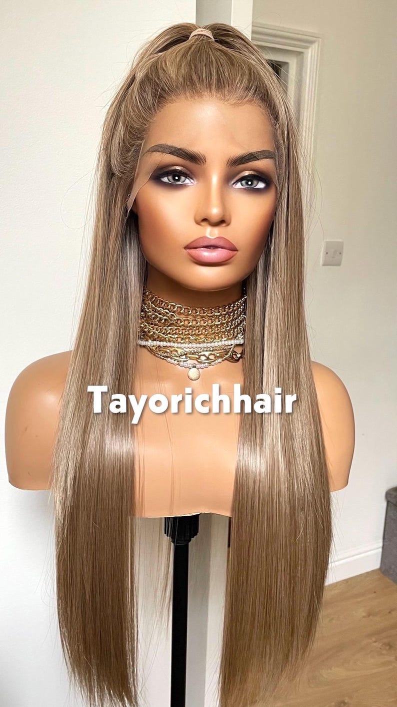May include: A long, straight, blonde wig on a mannequin head. The wig has a natural-looking hairline and is styled with a center part. The mannequin is wearing a gold necklace. The text "Tayorichhair" is displayed on the image.