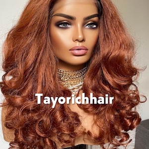 May include: A mannequin head displaying a long, wavy auburn wig. The wig features voluminous curls and a lace front. The text "Tayorichhair" is visible on the front. The model is wearing a gold necklace.