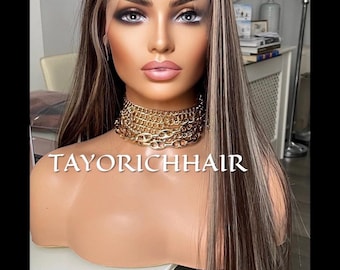 May include: A long, straight, brown wig with blonde highlights. The wig is styled with a center part and falls to the shoulders. The wig is worn by a mannequin with a gold chain necklace. The text "TAYORICHHAIR" is visible at the bottom of the image.