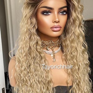 K&ouml;nnte beinhalten: Eine lange, blonde Per&uuml;cke mit lockeren, welligen Locken. Die Per&uuml;cke ist mit einem Mittelscheitel gestylt und hat einen nat&uuml;rlich aussehenden Haaransatz. Die Per&uuml;cke wird von einer Mannequin mit neutralem Gesichtsausdruck getragen.