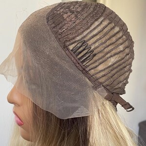 Puede incluir: Una peluca rubia con una parte delantera de encaje marr&oacute;n y una gorra marr&oacute;n. La peluca tiene pelo rubio largo y ondulado. La gorra tiene una parte delantera de encaje marr&oacute;n y una gorra marr&oacute;n con correas ajustables.