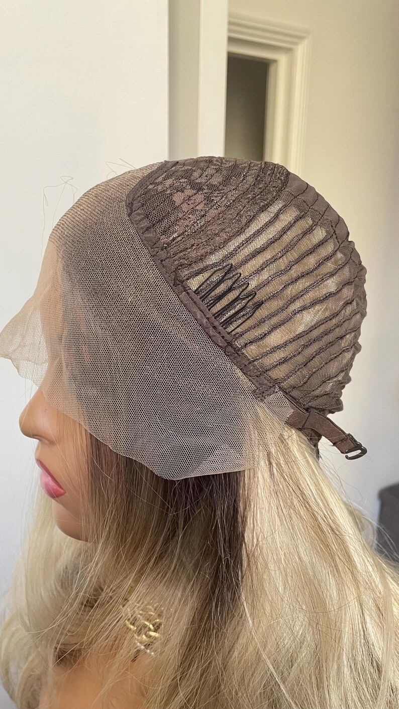 Puede incluir: Una peluca rubia con una parte delantera de encaje marr&oacute;n y una gorra marr&oacute;n. La peluca tiene pelo rubio largo y ondulado. La gorra tiene una parte delantera de encaje marr&oacute;n y una gorra marr&oacute;n con correas ajustables.