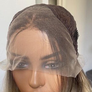 Puede incluir: Una peluca marr&oacute;n y rubia en una cabeza de maniqu&iacute;. La peluca presenta una parte delantera de encaje y una gorra marr&oacute;n oscuro. El cabello es una mezcla de tonos rubios y marrones. El maniqu&iacute; tiene labios rosados y un collar dorado.
