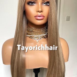 May include: A mannequin head displaying a long, straight wig with blonde and light brown highlights. The wig has a lace front and is styled with a center part. The text "Tayorichhair" is visible on the mannequin.