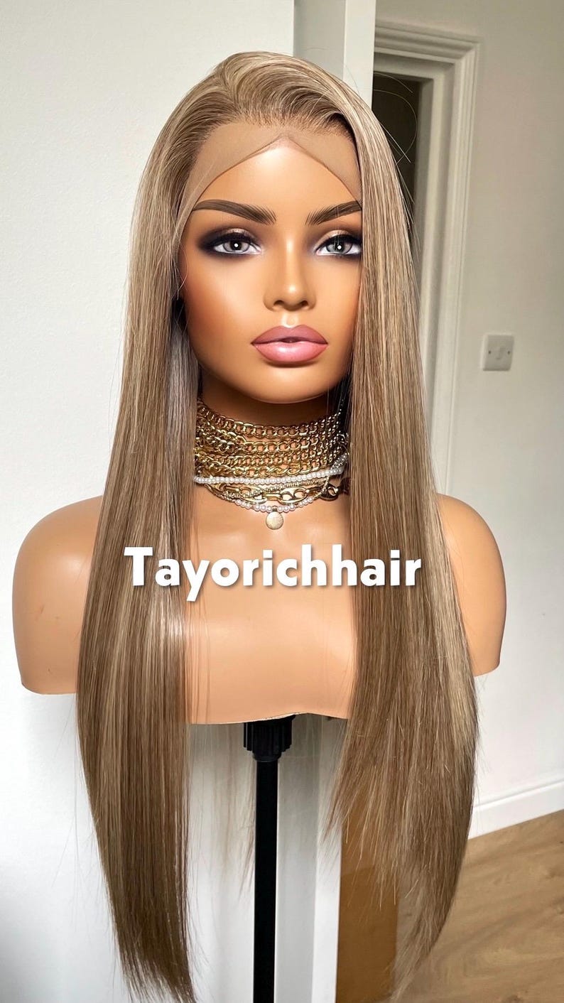 May include: A mannequin head displaying a long, straight wig with blonde and light brown highlights. The wig has a lace front and is styled with a center part. The text "Tayorichhair" is visible on the mannequin.
