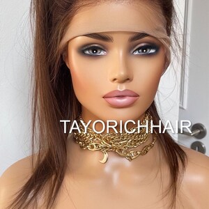 May include: A long, straight, brown human hair wig with a lace front. The wig is styled in a high ponytail. The wig is on a mannequin head. The mannequin is wearing a gold chain necklace with a crescent moon pendant. The text "TAYORICHHAIR" is visible on the mannequin's chest.