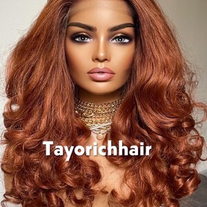 May include: A mannequin head with a copper-colored, wavy wig. The wig has a lace front and is styled with voluminous curls. The text "Tayorichhair" is displayed at the bottom of the image. A gold necklace is around the mannequin's neck.