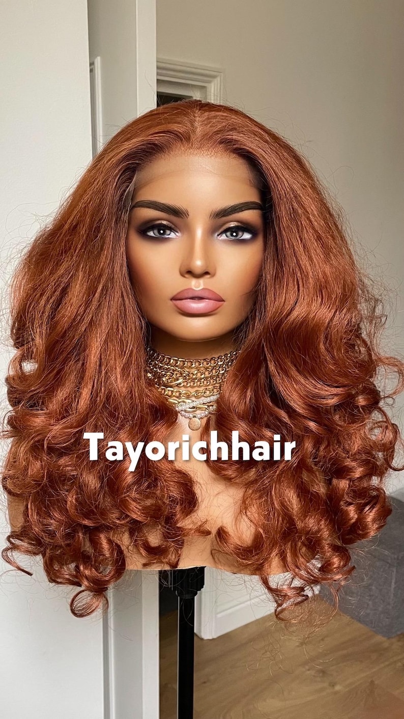 May include: A mannequin head with a copper-colored, wavy wig. The wig has a lace front and is styled with voluminous curls. The text "Tayorichhair" is displayed at the bottom of the image. A gold necklace is around the mannequin's neck.