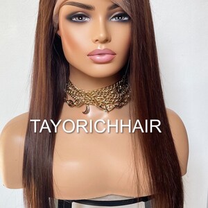 May include: A long, straight, brown human hair wig with a lace front. The wig is styled with a side part and is worn on a mannequin head. The mannequin is wearing a gold chain necklace with a crescent moon charm. The text "TAYORICHHAIR" is visible on the mannequin's chest.