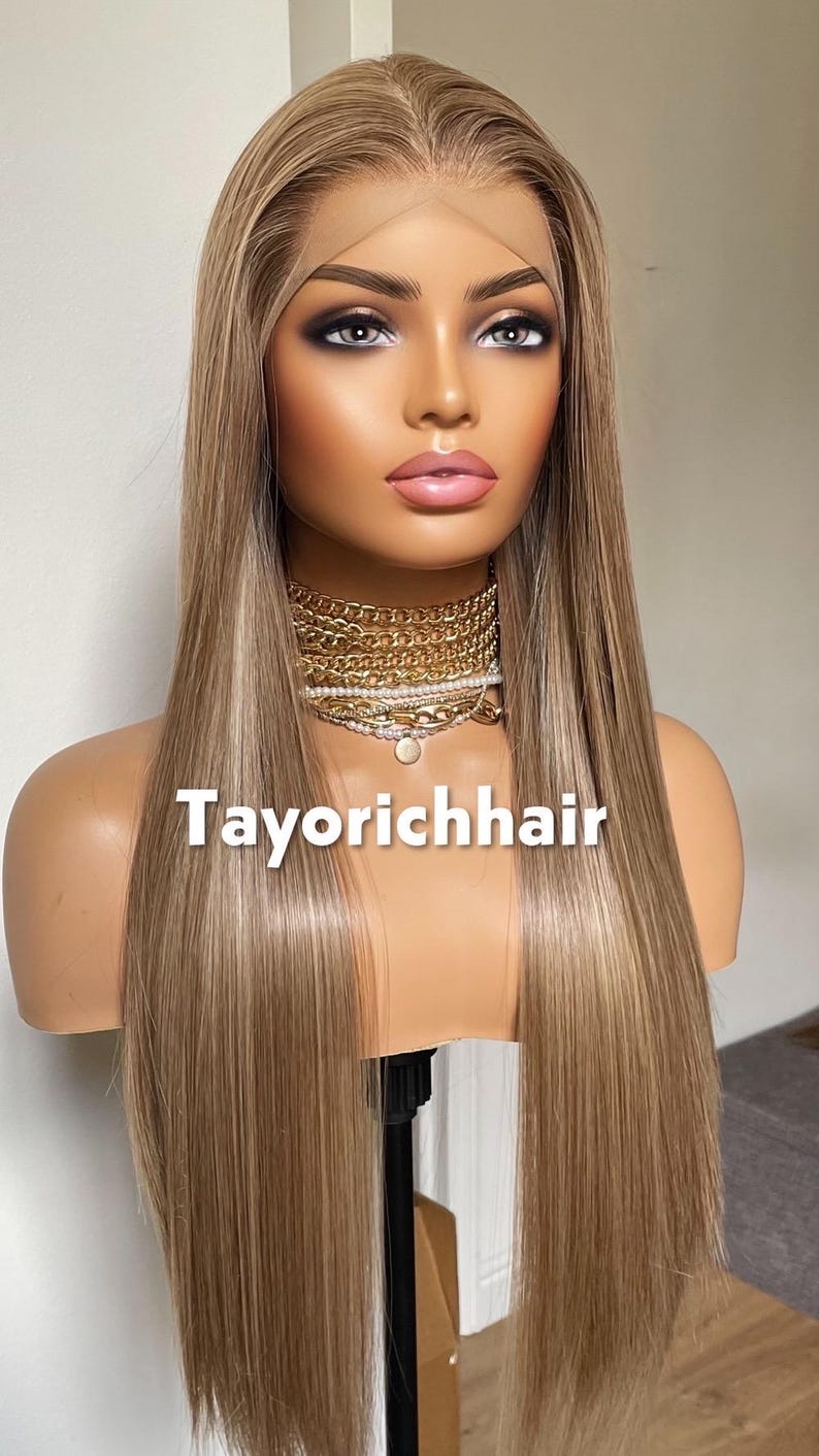 May include: A long, straight blonde wig with highlights is displayed on a mannequin head. The wig features a lace front and is styled with a center part. The mannequin is wearing a gold necklace. The text "Tayorichhair" is printed on the mannequin.