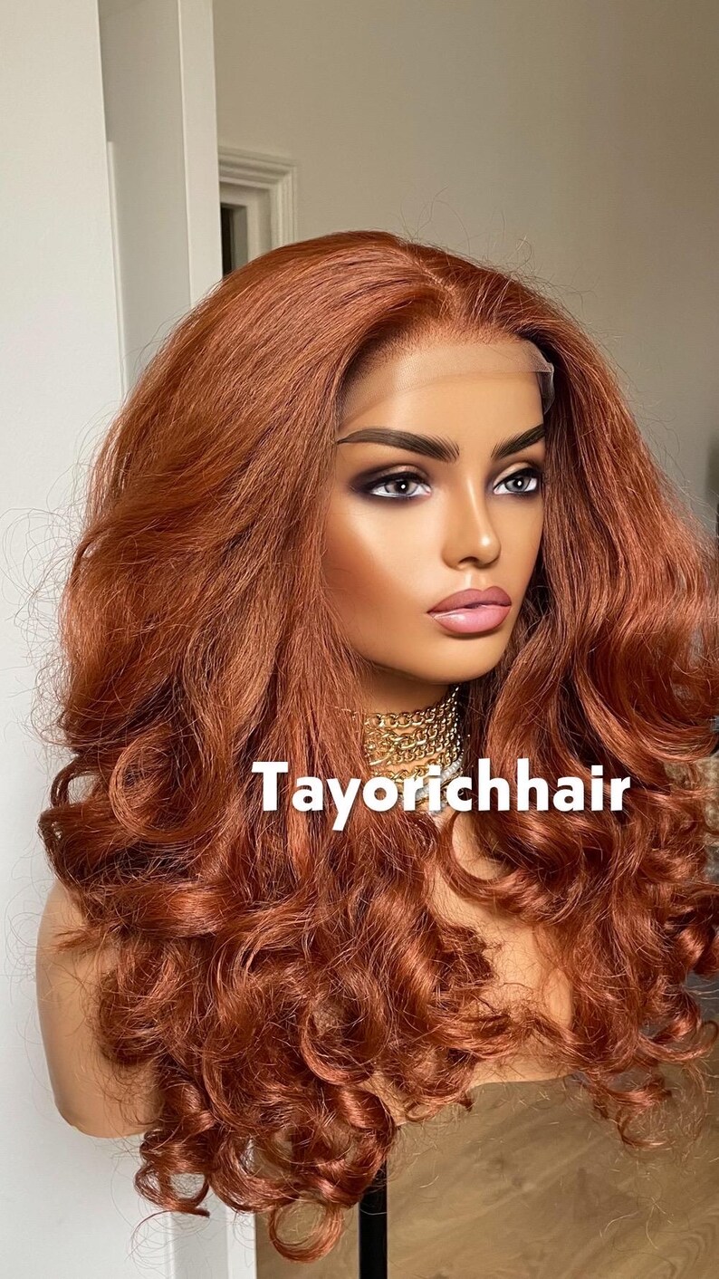 May include: A mannequin head displaying a long, wavy auburn wig. The wig features a lace front and voluminous curls. A gold chain necklace is visible. The text "Tayorichhair" is displayed on the image.