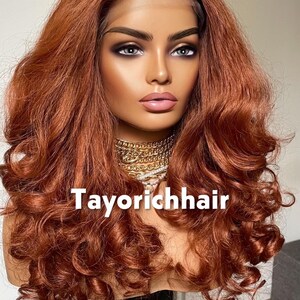 May include: A mannequin head displaying a long, wavy auburn wig. The wig features voluminous curls and a lace front. The text "Tayorichhair" is visible at the bottom. The model is wearing a gold necklace.