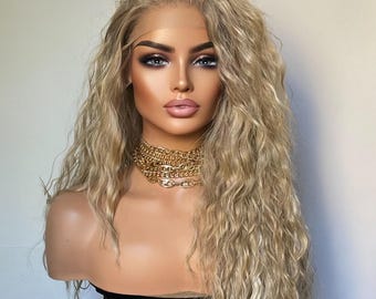 Op de afbeelding: Een lange, golvende, lichtblonde pruik met een natuurlijke scheiding. De pruik is gestyled in losse golven en heeft een natuurlijke, licht rommelige look.