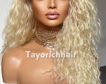 Puede incluir: Una peluca rubia larga y rizada con raíces oscuras sobre una cabeza de maniquí. El cabello presenta un frente de encaje y una textura ondulada voluminosa. El maniquí lleva un collar de cadenas doradas. El texto Tayorichhair es visible en la imagen.
