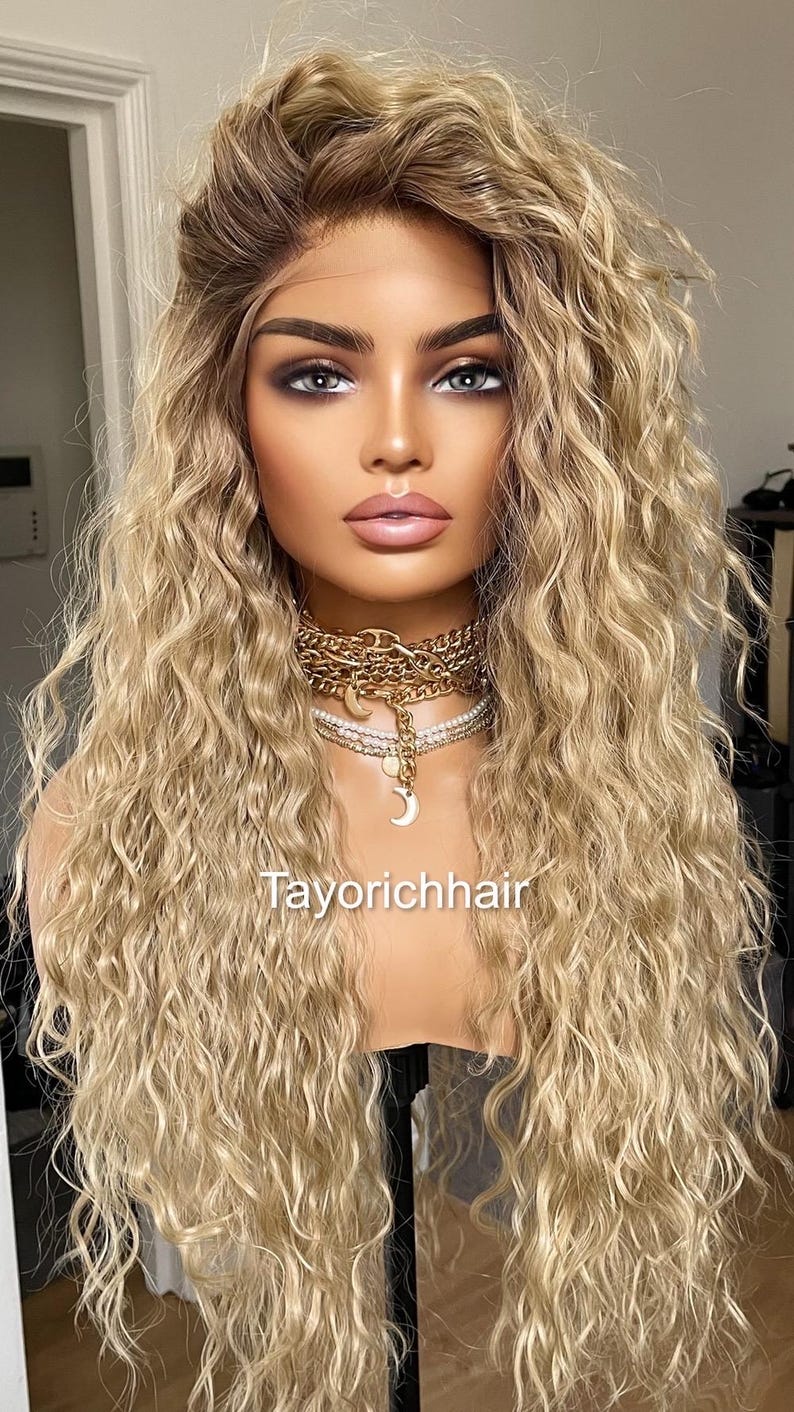 K&ouml;nnte beinhalten: Eine lange, blonde Per&uuml;cke mit lockeren, lockigen Wellen. Die Per&uuml;cke ist auf einem Mannequin-Kopf gestylt und hat einen nat&uuml;rlich aussehenden Haaransatz.
