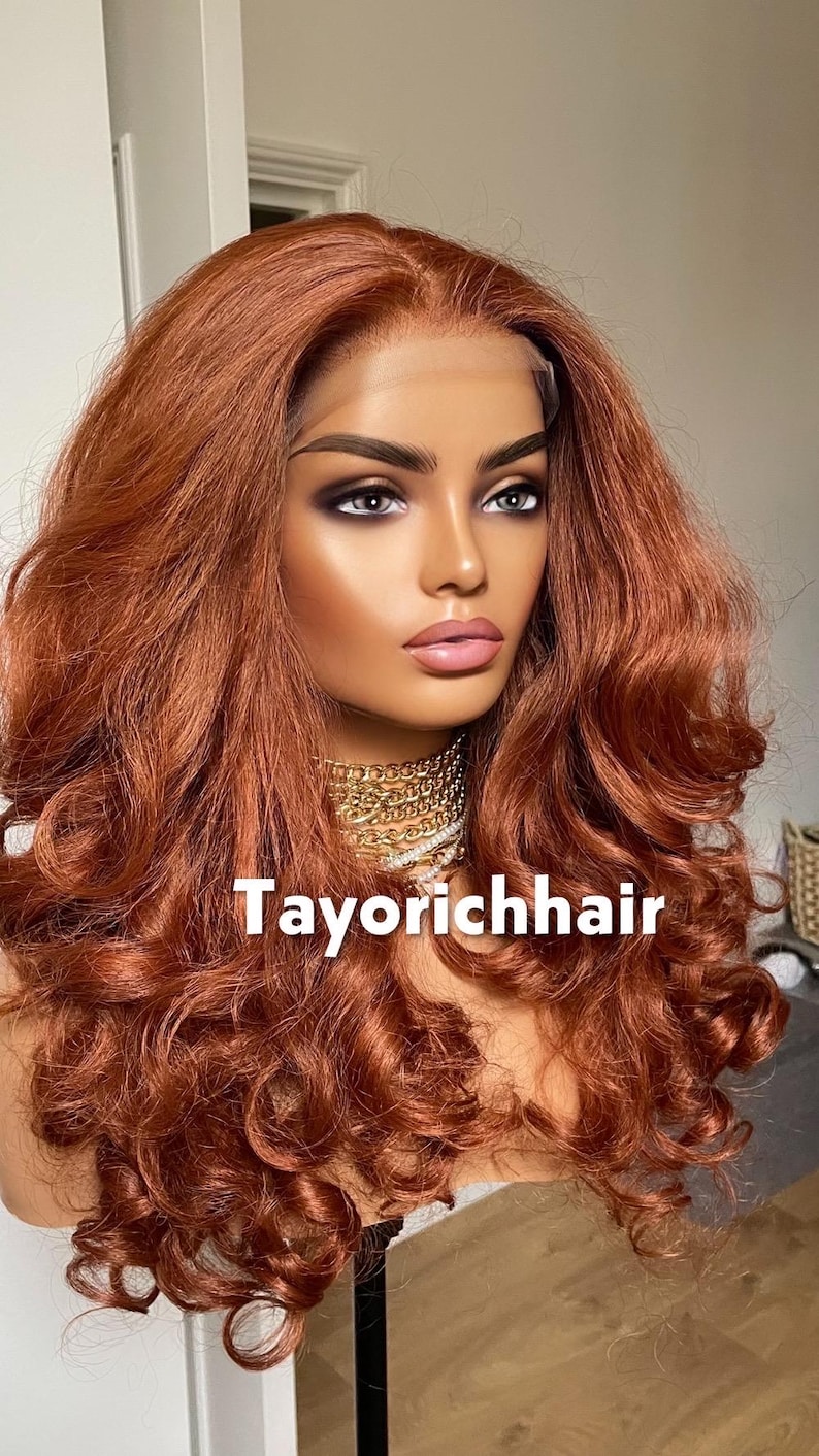 May include: A mannequin head with a copper-colored, wavy wig. The wig features long, voluminous curls and a lace front. The mannequin is wearing a gold chain necklace. The text "Tayorichhair" is displayed on the image.