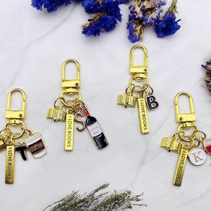May include: Four gold keychains with different charms. Each keychain has a gold charm with the text "I LOVE BOOKS". The charms include a book, a wine bottle, a coffee cup, and a wine glass.