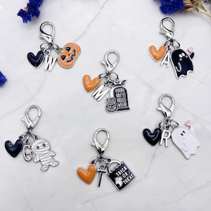 May include: A collection of Halloween-themed charms with silver-tone clasps. Charms include a jack-o'-lantern, ghost, mummy, and a tombstone with the text "Every Day is Halloween". Other charms include hearts, letters, and a trick-or-treat bag.