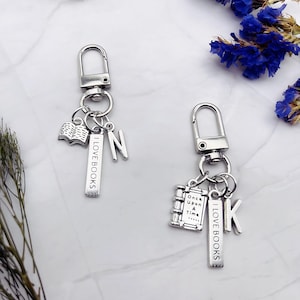 May include: Two silver keychains with charms. One keychain has a charm that says "I love books" and a charm with the letter "N". The other keychain has a charm that says "I love books" and a charm that says "Once upon a time..." and a charm with the letter "K".