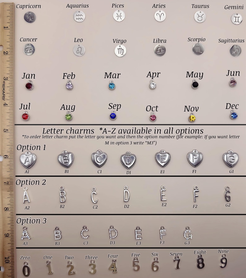 May include: A display board featuring zodiac symbols, birthstone charms for each month, and letter charms in three styles labeled A1 through G3, alongside number charms zero through nine. A 10-inch ruler is positioned vertically on the left side.
