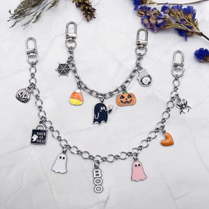 May include: Silver-toned chain accessories with Halloween-themed charms. Charms include a pumpkin, ghost, spider, candy corn, and a lock with "Trick or Treat" text. The chains have lobster clasp closures.