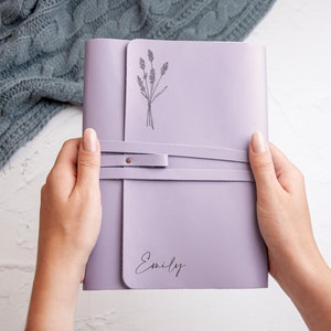 May include: A lavender-colored leather journal with a simple drawing of lavender flowers and the name "Emily" embossed on the front cover.