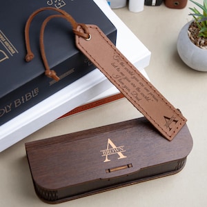 May include: A brown wooden box with a laser engraved letter "A" and the word "BROWN" on the lid. The box is open and a brown leather bookmark with a personalized message is inside. The bookmark has a leather strap and a metal ring.