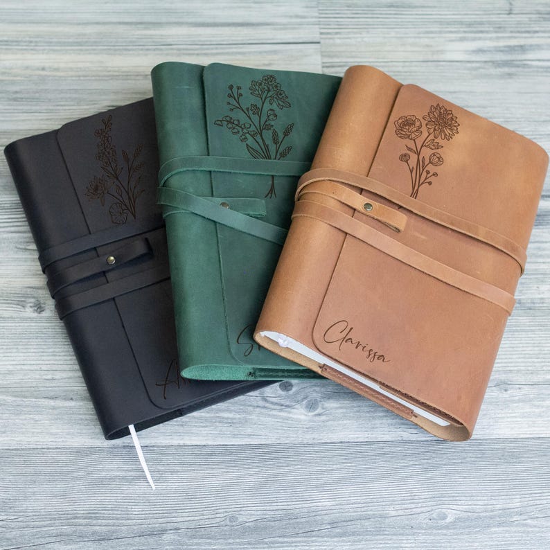 May include: Three leather-bound journals with floral designs and personalized names. The journals are in black, green, and brown.