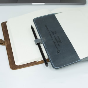 May include: A brown leather journal with a blue leather cover. The blue cover has a quote from Romans 12:12 inscribed on it. "Rejoice in hope, be patient in tribulation, be constant in prayer Romans 12:12"
