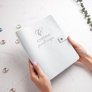 A person's hands holding a white notebook with the word "Cynthia" printed on it.