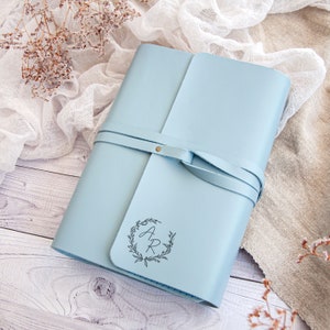 May include: A light blue leather journal with a leather strap closure and a monogrammed wreath with the initials "A.R." in a cursive font.
