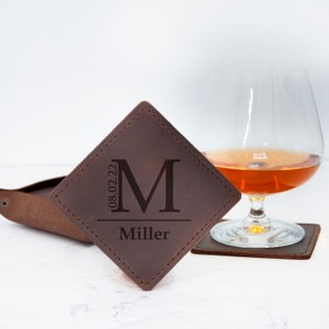 May include: Brown leather coaster with a monogrammed initial "M" and the name "Miller" and the date "08.02.22" engraved on it.