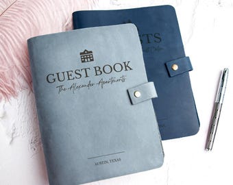 May include: Two leather guest books, one light blue and one navy blue, with silver pen. The light blue book is embossed with "GUEST BOOK" and "The Alexander Apartments" and "AUSTIN, TEXAS". The navy blue book has text on the cover.