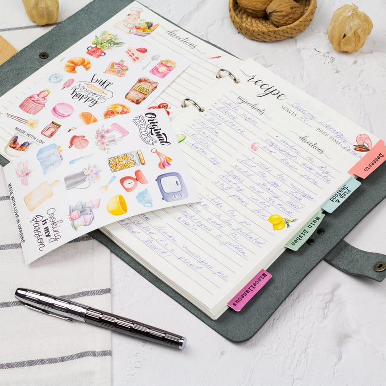 a notebook with handwritten recipes, a pen, and various kitchen-related items such as a bowl, a spoon, and a basket of nuts.