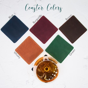 May include: Six leather coasters in different colors: blue, burgundy, brown, whisky, green. The coasters are square and have a stitched edge. The coasters are arranged in a circle around a glass of amber liquid.