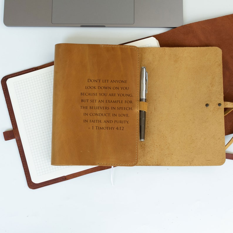 May include: A brown leather journal with a pen tucked into the pocket. The journal has an inspirational quote from 1 Timothy 4:12 engraved on the front cover: "Don't let anyone look down on you because you are young. But set an example for the believers in speech, in conduct, in love, in faith, and purity. - 1 Timothy 4:12"