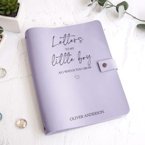K&ouml;nnte beinhalten: Ein lavendelfarbenes Notizbuch mit dem Text "Letters to my little boy as I watch you grow" und dem Namen "Oliver Anderson" auf dem Einband. Das Notizbuch hat einen Druckknopfverschluss.