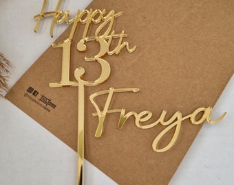 Puede incluir: Topper para pastel de acrílico dorado con las palabras "Happy 13th Freya" en una fuente cursiva.