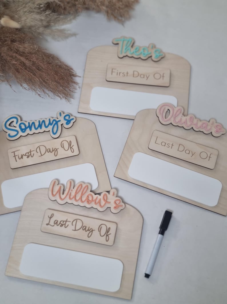May include: Four wooden signs with white paint and a blank space for writing. Each sign has a name written in colorful letters and a phrase that says "First Day Of" or "Last Day Of". A black marker is included.