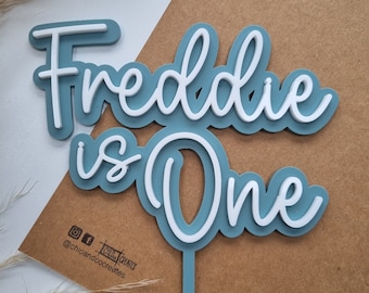 May include: Blue and white acrylic cake topper with the text "Freddie is One".