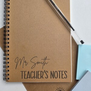 May include: A spiral-bound notebook with a kraft paper cover. The cover features the text "Mr Smith TEACHER'S NOTES" in black. A clear pen rests on the notebook. The bottom right corner shows the logo "chloe&co CREATES".