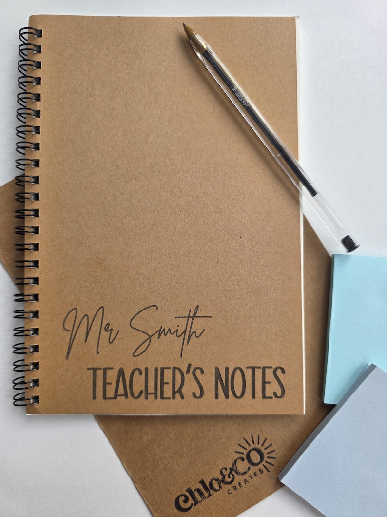 May include: A spiral-bound notebook with a kraft paper cover. The cover features the text "Mr Smith TEACHER'S NOTES" in black. A clear pen rests on the notebook. The bottom right corner shows the logo "chloe&co CREATES".