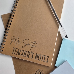 May include: A spiral-bound notebook with the text "Mr Smith TEACHER'S NOTES" in black script. A clear pen rests on the notebook. The notebook is on top of a brown paper and light blue sticky notes. The logo "chloe&co CREATES" is visible.